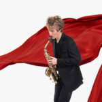 Signature Symphony Artistic Director plays a saxophone in front of a fluttering red banner.